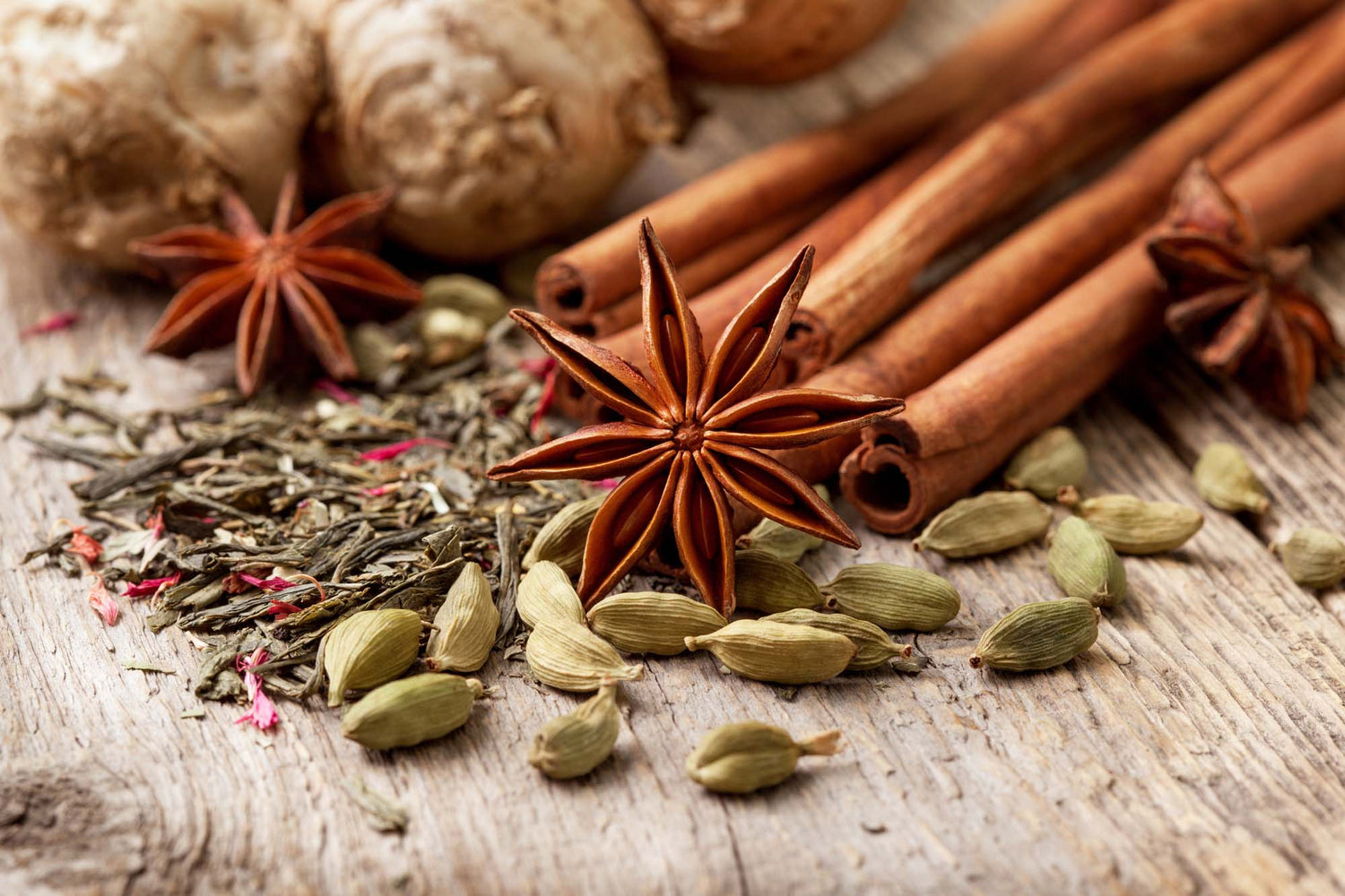 Spices including cinnamon sticks, star anise, and cardamom pods on a wooden surface